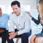 therapist and a spouse consoling the other spouse sitting on couch